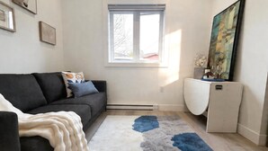 A living room with a sofa, a rug, a window, and a painting on the wall. - Vancouver Katherine 2BD 2BA Laneway Home (Vancouver)