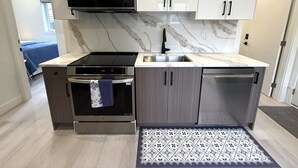 A modern kitchen with a built-in microwave, oven, and dishwasher, marble backsplash, and light wood cabinets. - Vancouver Katherine 2BD 2BA Laneway Home (Vancouver)