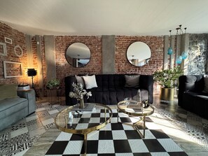 A living room with a black sofa, round mirrors, a checkered floor, and a brick wall.