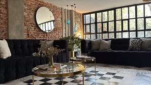 A living room with a black sofa, a round coffee table, and a large window with a view of trees.