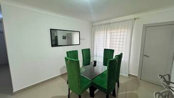 A dining area with a glass table surrounded by green upholstered chairs, a white door, and a mirror on the wall.