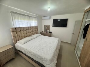 A bedroom with a bed, bedside table, wardrobe, and a TV on the wall. - Luxury apartment  (San Francisco de Macorís)