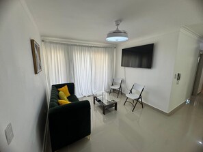 A modern living room with a sofa, two chairs, a glass coffee table, a flat-screen TV, and a ceiling fan. - Luxury apartment  (San Francisco de Macorís)