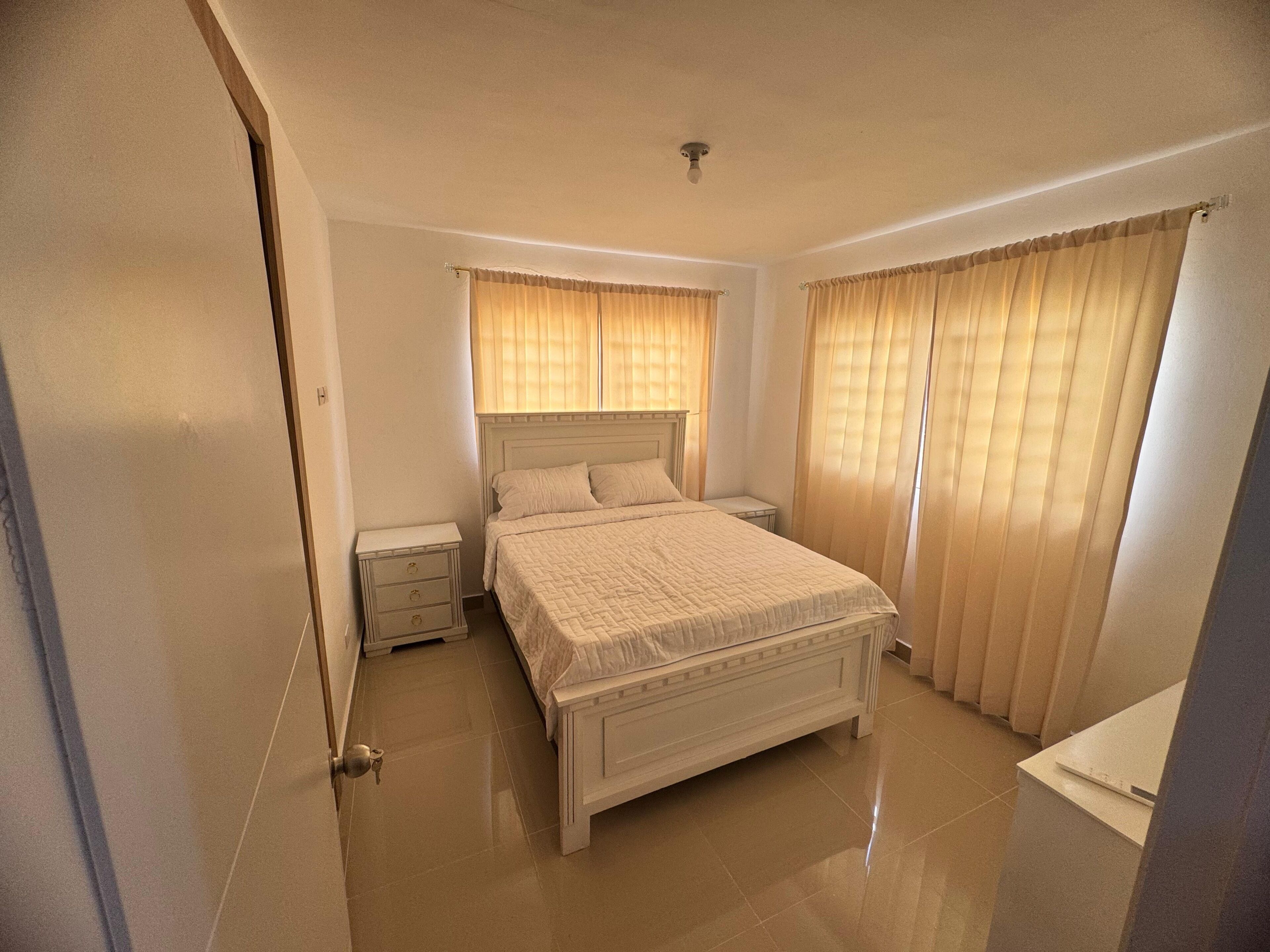 Ein Schlafzimmer mit Bett, Nachttischen, Schreibtisch und Vorhängen.