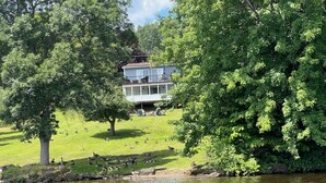 Une maison avec une pelouse et un étang, entourée d’arbres.