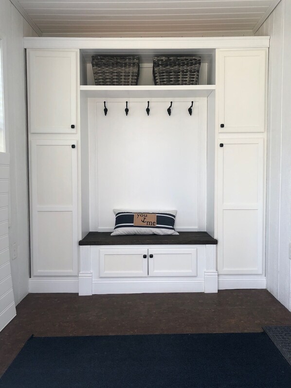 A white built-in bench with a pillow, hooks, and baskets.