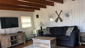 Un salon avec un canapé foncé, une table basse en bois, un téléviseur et un tableau encadré représentant deux pagaies croisées.