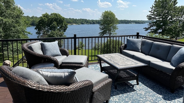 Une terrasse dotée de meubles en osier, d’une table et offrant une vue sur un lac.