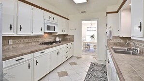 Una cocina con armarios blancos, microondas y lavamanos.