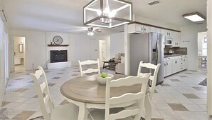 Una cocina amplia con armarios blancos, una mesa de comedor con sillas y una lámpara central.
