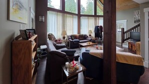 Ein gemütliches Wohnzimmer mit hohen Decken, großen Fenstern, einem Kamin und einem Fernseher.
