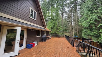 A wooden deck leading to a house with a sliding glass door, surrounded by a forest.