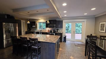 A modern kitchen with a central island, dark cabinetry, and a dining area with chairs.