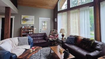 A spacious living room with a high ceiling, large windows, and a cozy fireplace.
