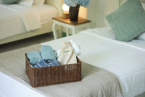 A neatly made bed with a wicker basket containing towels and a bag on the bed.