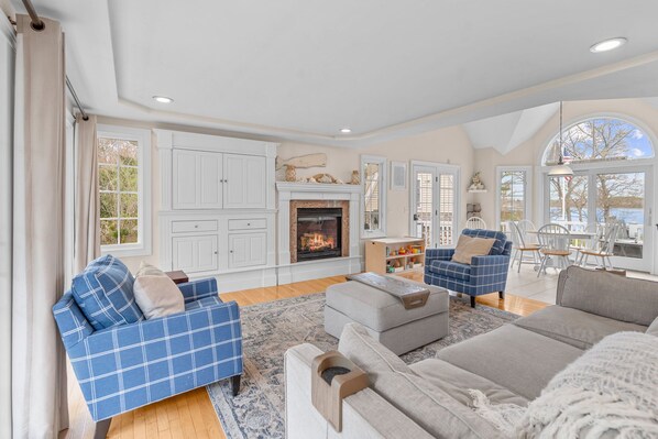 A spacious living room with a fireplace, blue and grey sofas, and a view of the outdoors.