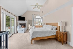 A bedroom with a large bed, a TV, a fireplace, and a balcony.