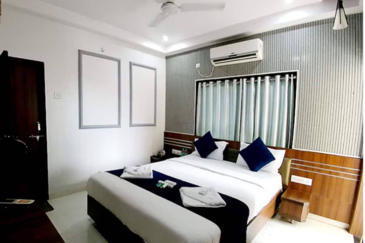 Una habitación de hotel con cama, mesitas de noche, equipo de aire acondicionado y ventilador de techo.
