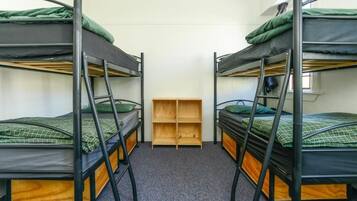 Een kamer met drie stapelbedden, een houten schapenkast en een vloerbedekking.