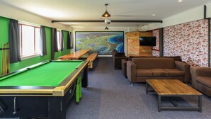 A pool table, sofas, a TV, and a mural in a room with green walls and a wooden ceiling. - The Rotten Apple Back Packers (Hastings)
