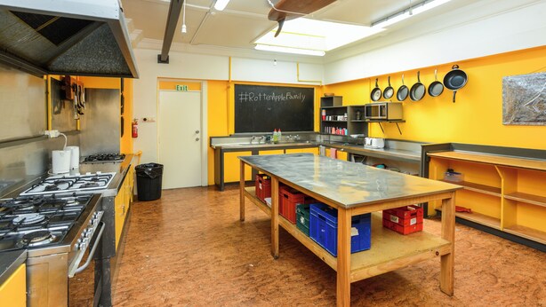 A kitchen with a stove, sink, and chalkboard with #PottenAppleFamily. - The Rotten Apple Back Packers (Hastings)