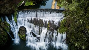A waterfall cascading over rocks surrounded by dense greenery. - The Rotten Apple Back Packers (Hastings)