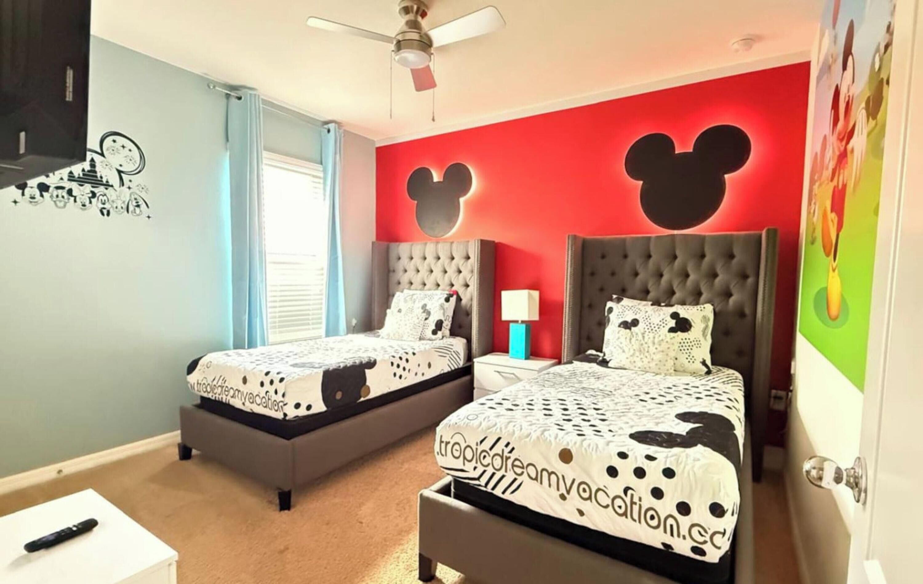 A bedroom with two beds, a ceiling fan, and a Mickey Mouse wall decal.