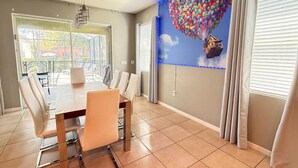 Un comedor con mesa y sillas, un ventanal con persianas y un mural en la pared.