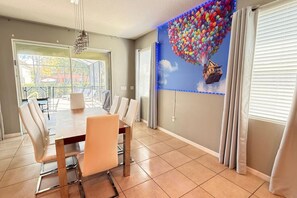 A dining area with a table and chairs, a large window with blinds, and a mural on the wall. - Sunset Swims Disney Dreams-modern Family Oasis (Davenport)