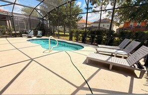 A covered outdoor swimming pool with lounge chairs, a pool ladder, and a view of houses in the background. - Sunset Swims Disney Dreams-modern Family Oasis (Davenport)