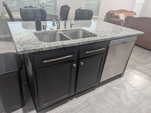 Una cocina con encimeras de granito, un lavamanos doble, armarios negros y lavavajillas.