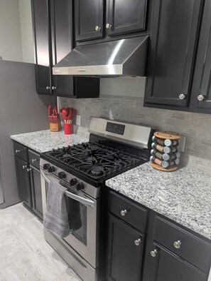 A kitchen with a stainless steel stove, black cabinets, granite countertops, and a built-in oven. - Cozy 3BR-2BA Near Downtown/NRG Med Center + WiFi (Houston)