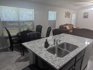 A modern kitchen with granite countertops, stainless steel sink, and black chairs. - Cozy 3BR-2BA Near Downtown/NRG Med Center + WiFi (Houston)