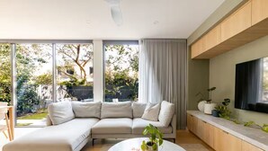 Een moderne woonkamer met een hoekbank, een bijzettafeltje met een plant en een aan de muur bevestigde televisie.