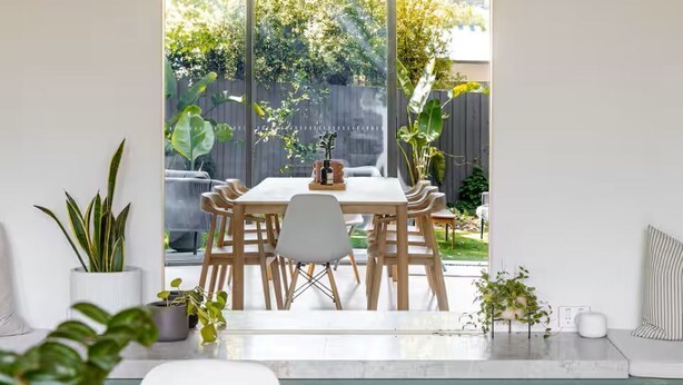 Een eetruimte met een tafel en stoelen, een groot rondboogvenster en potplanten.