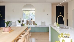 Een moderne keuken met een marmeren aanrecht, een wastafel met gouden kraan, en een eethoek met een houten tafel en stoelen.