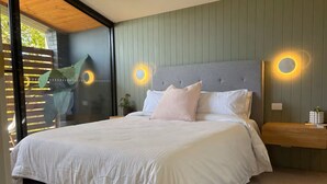 Een moderne slaapkamer met een groot bed, twee wandlampen, een houten bankje en uitzicht door een glazen deur.
