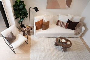 Una sala de estar moderna con un sofá blanco, un sillón, una mesita de centro, una lámpara de pie y una planta verde grande.