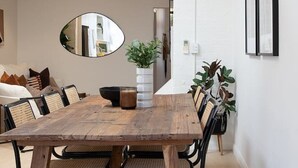 Un coin repas avec une table en bois, des chaises noires, une suspension blanche et un miroir au mur.