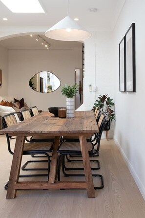 Un comedor con una mesa de madera, sillas negras, una lámpara colgante blanca y un espejo en la pared.
