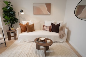 A modern living room with a white sofa, multiple cushions, a small wooden side table, a floor lamp, and a large potted plant. - Chic 3BR Family Home with rare Garden & Parking (Surry Hills)