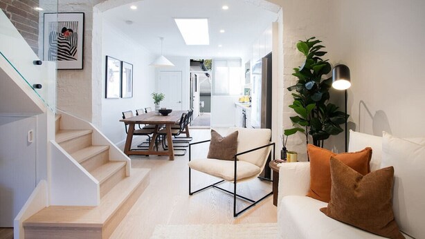 Un intérieur moderne comprenant un escalier, un coin repas et un salon avec un canapé et des coussins.