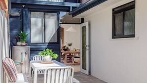 Un petit patio extérieur avec une table et des chaises blanches, un chauffe-eau et une porte donnant sur un espace intérieur.