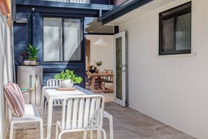 Un pequeño patio exterior con una mesa y sillas blancas, un calentador de agua y una puerta que da a un espacio interior.