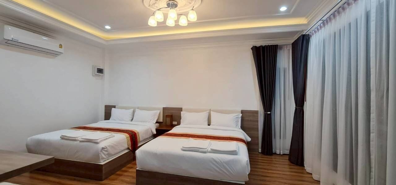 A hotel room with two beds, a ceiling light fixture, an air conditioning unit, and a window with curtains.