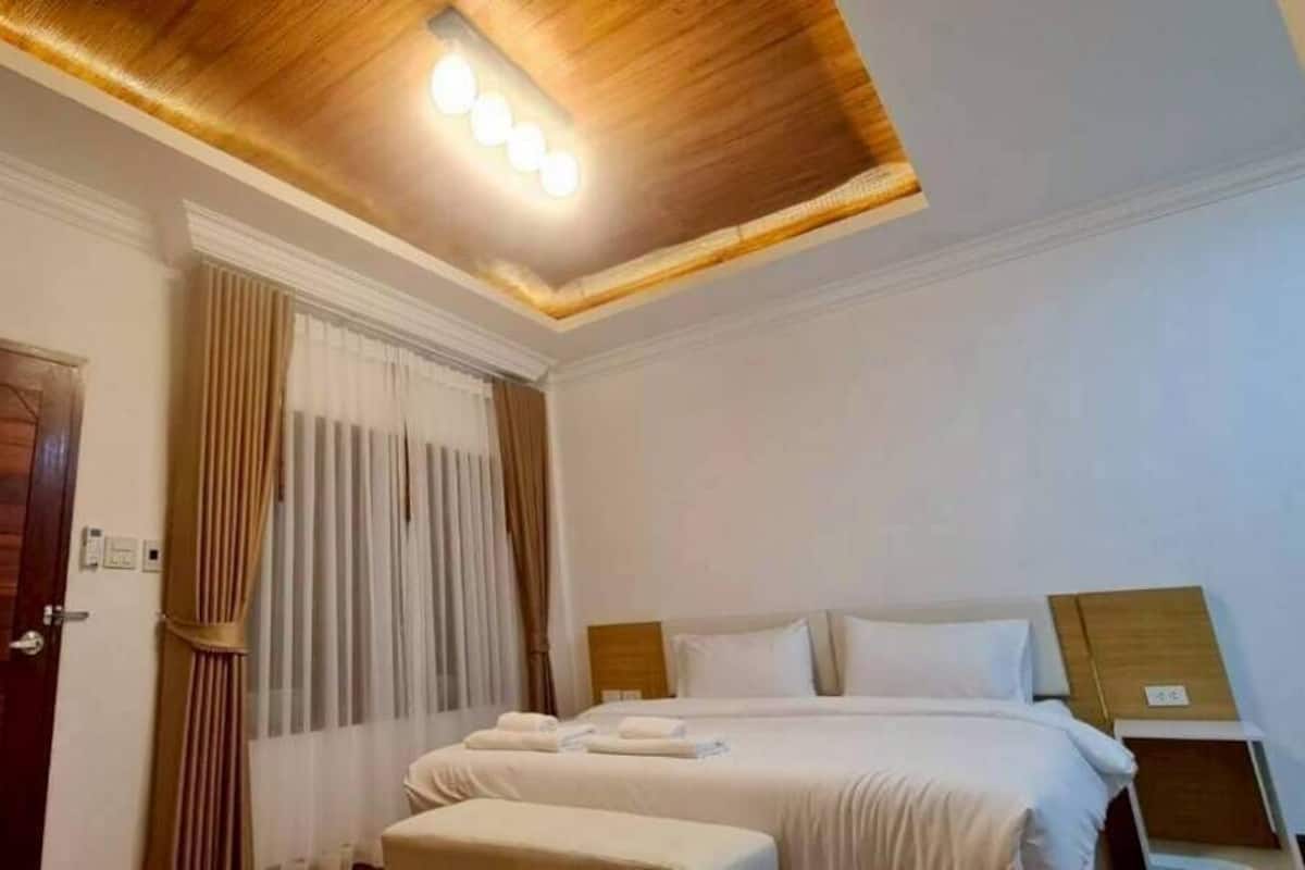 Una habitación de hotel con techo de madera, una cama con sábanas blancas, una mesita de noche y una puerta.