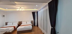 Een hotelkamer met twee bedden, een houten vloer, een plafondlamp en gordijnen.