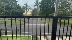 A balcony with a view of a road, a parking area, and a beach in the distance. - Spacious modern Beachside 2 Bedroom Unit. (Pialba)