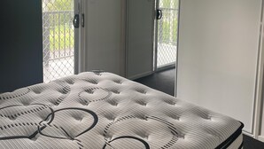 A bedroom with a bed, ceiling fan, air conditioning unit, and a sliding glass door leading to a balcony. - Spacious modern Beachside 2 Bedroom Unit. (Pialba)