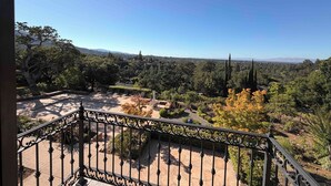 A balcony with a wrought iron railing overlooking a landscaped garden and distant mountains.